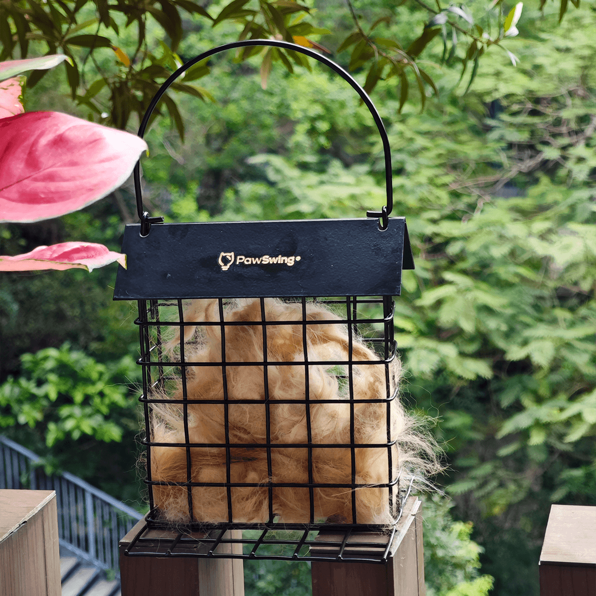 An outdoor scene featuring the PawSwing® eco friendly cat hair reuse station hanging amidst green foliage