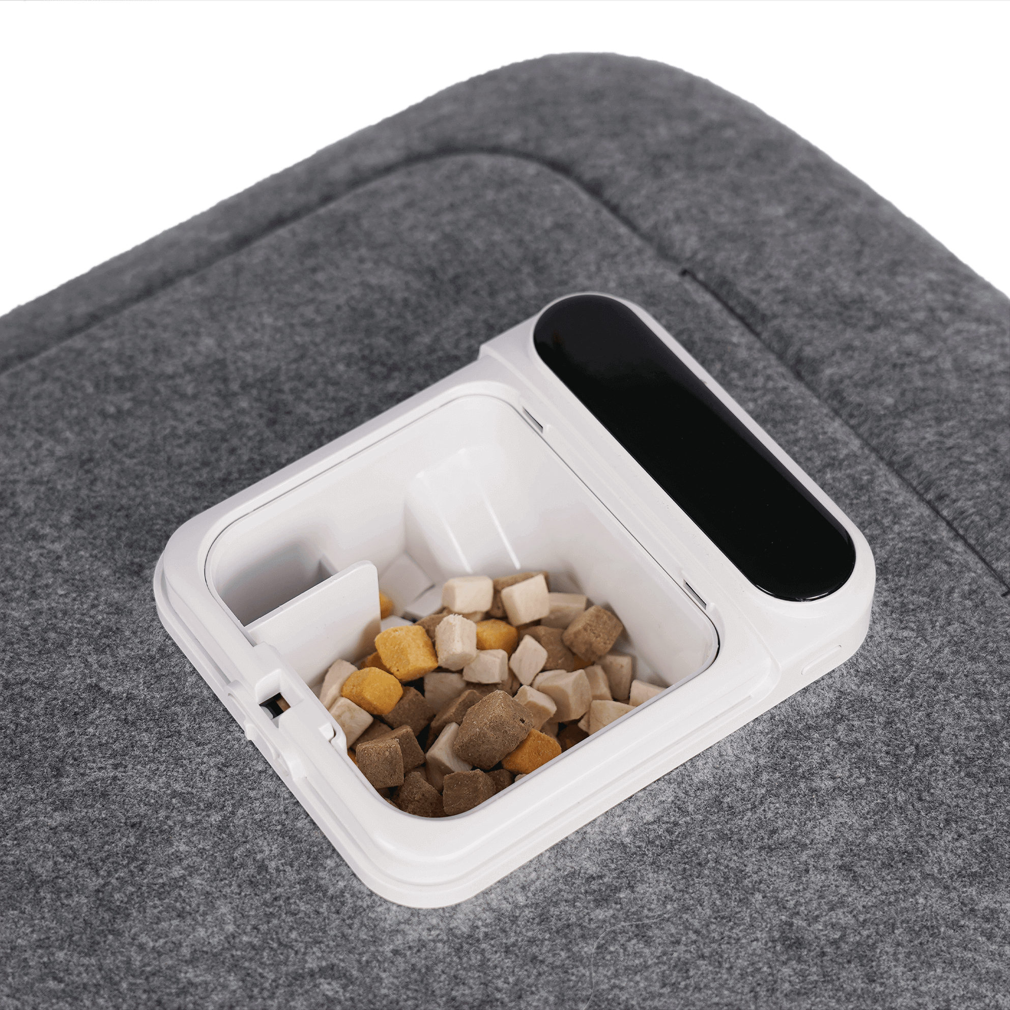 Container with kibble for pet grooming tool on a gray fabric surface.