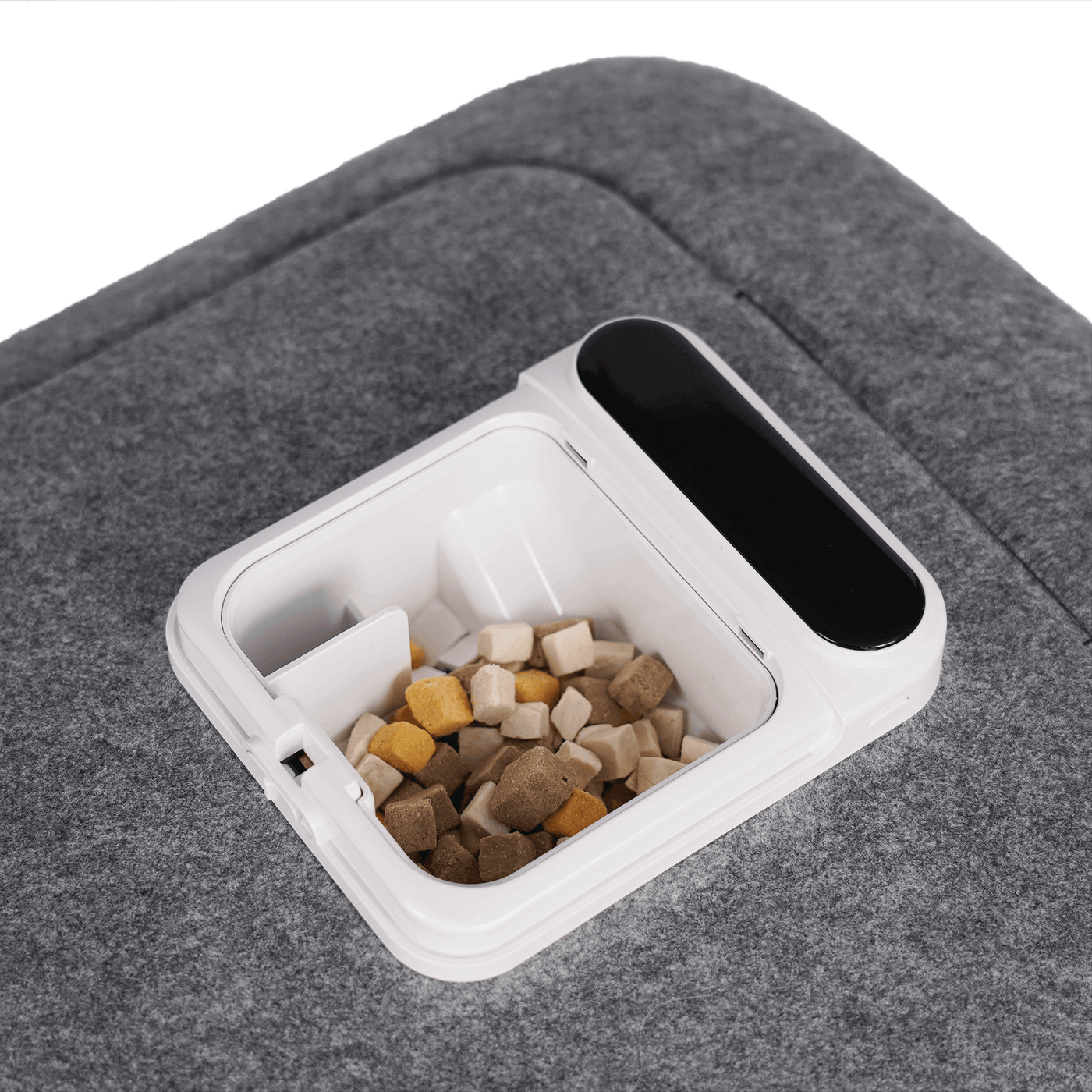 Container with kibble for pet grooming tool on a gray fabric surface.
