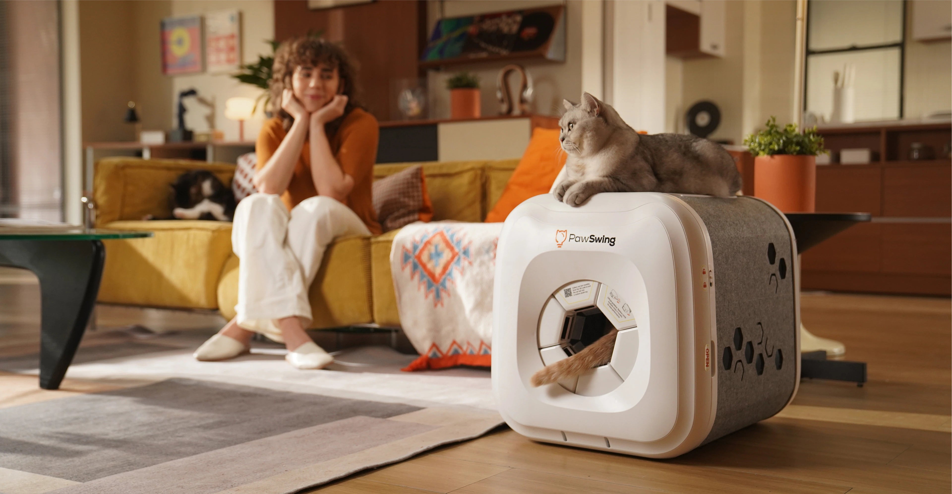 A cat resting on a PawSwing® neo self grooming cat house while another cat’s tail peeks from inside